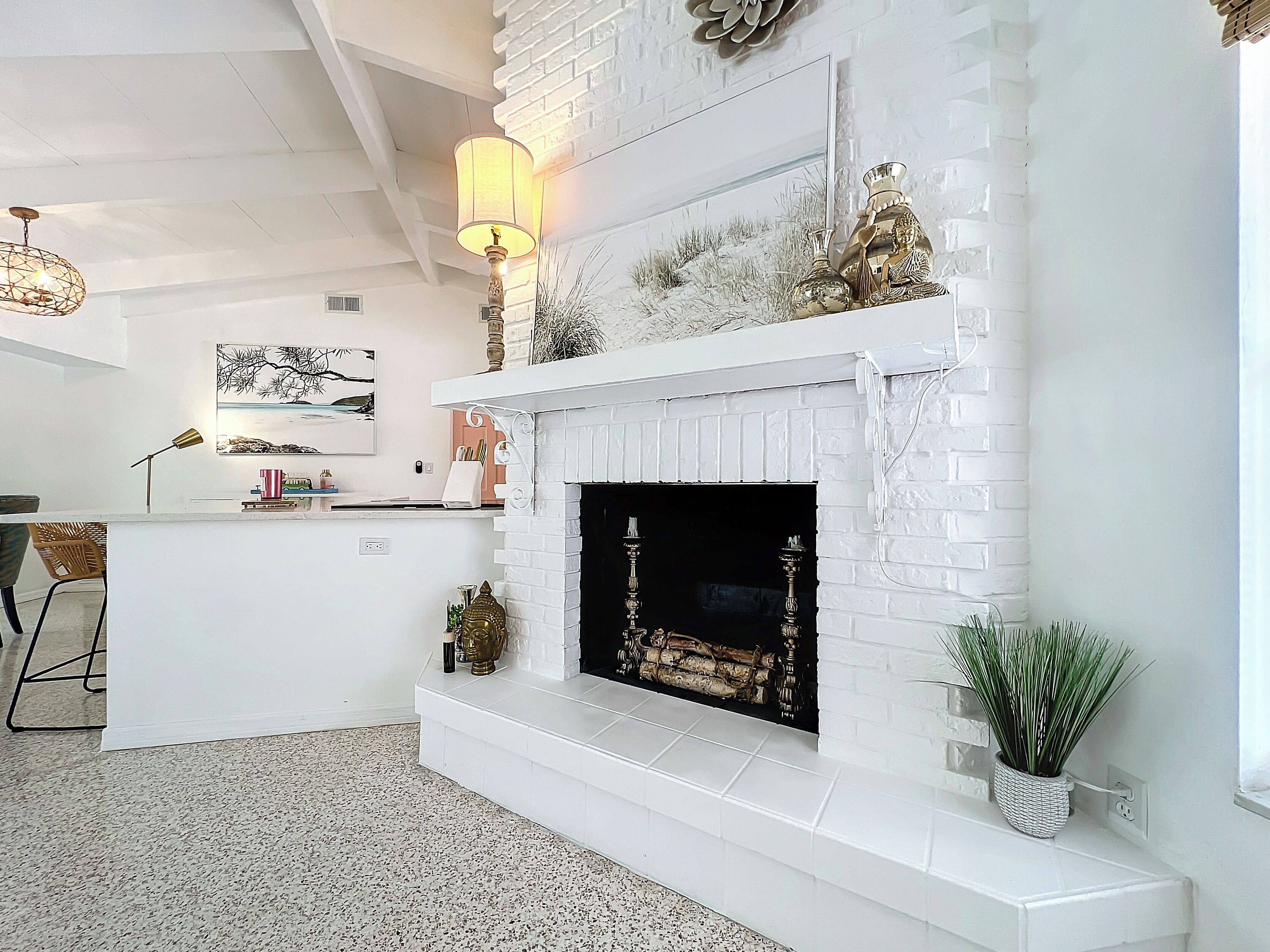 A modern living room with a white brick fireplace, a dining area with a white countertop, and a large window providing natural light.