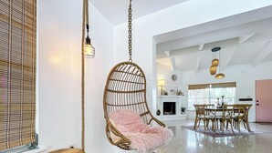 Un vaste espace de vie comprenant un fauteuil suspendu, une table en bois, un pouf à motifs et un ensemble de salle à manger.