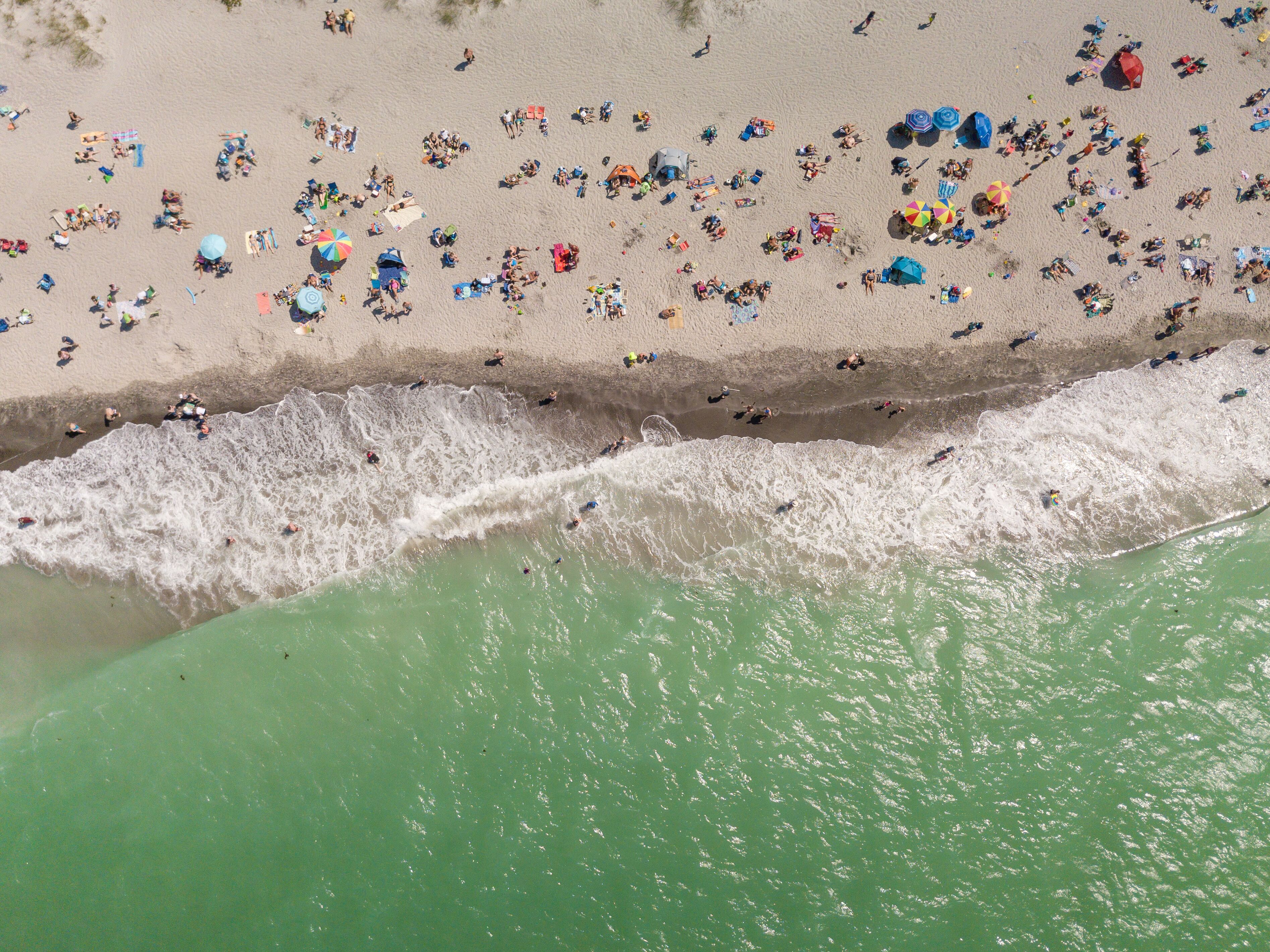 Vista aérea de una playa con gente, sombrillas y sillas de playa.
