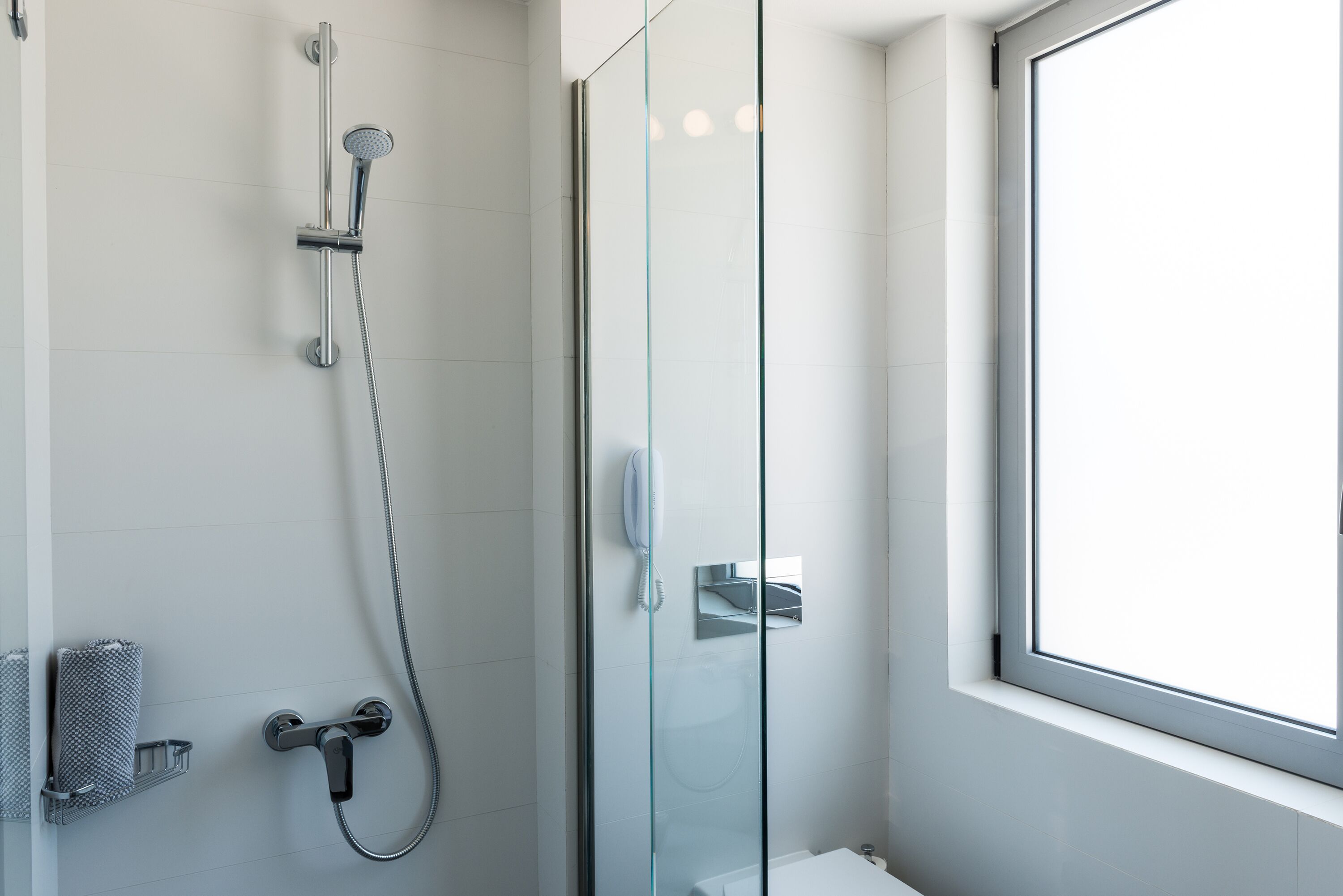 A modern bathroom with a glass shower enclosure, a toilet, and a window providing natural light.