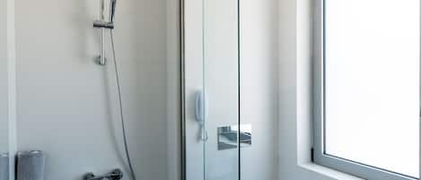 A modern bathroom with a glass shower enclosure, a toilet, and a window providing natural light.