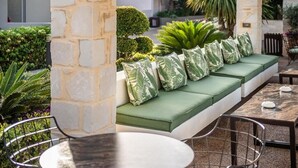 Un pilar de piedra, un banco verde con cojines estampados y una mesa redonda con sillas.