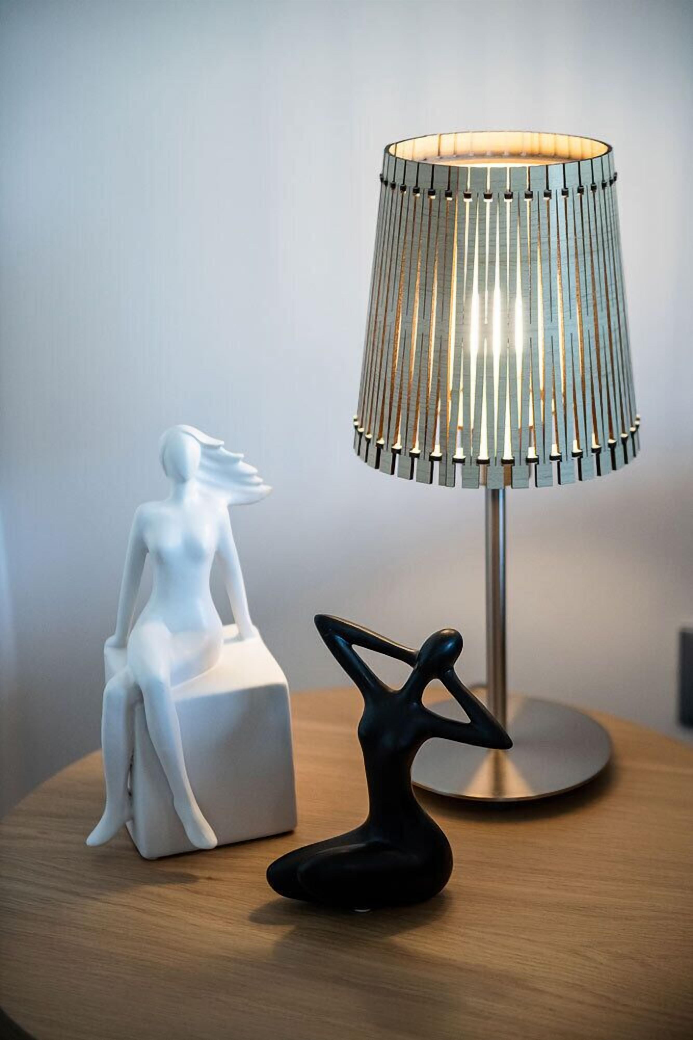 A modern lamp with a ribbed design on a wooden table next to a white sculpture and a black abstract sculpture.