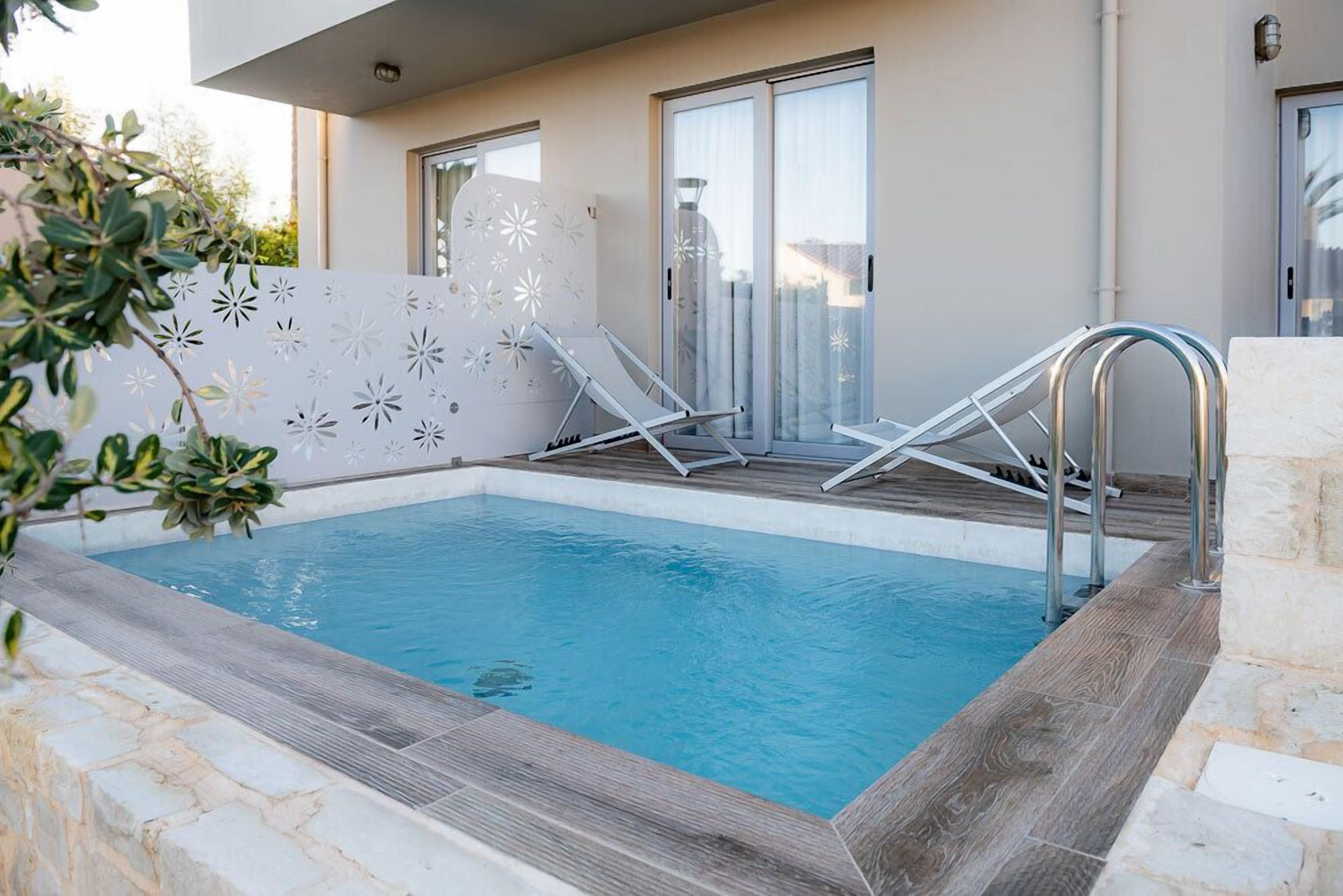 A modern outdoor swimming pool with two lounge chairs and a glass balustrade.