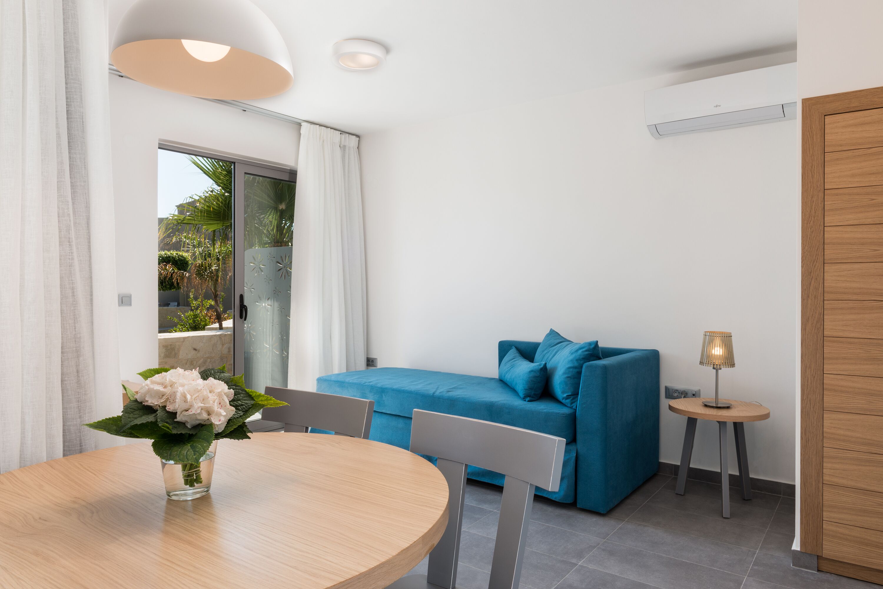 A modern room with a round wooden table, a blue sofa, and a small side table with a lamp.