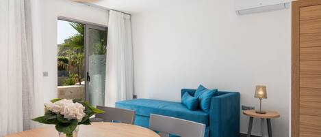A modern room with a round wooden table, a blue sofa, and a small side table with a lamp.