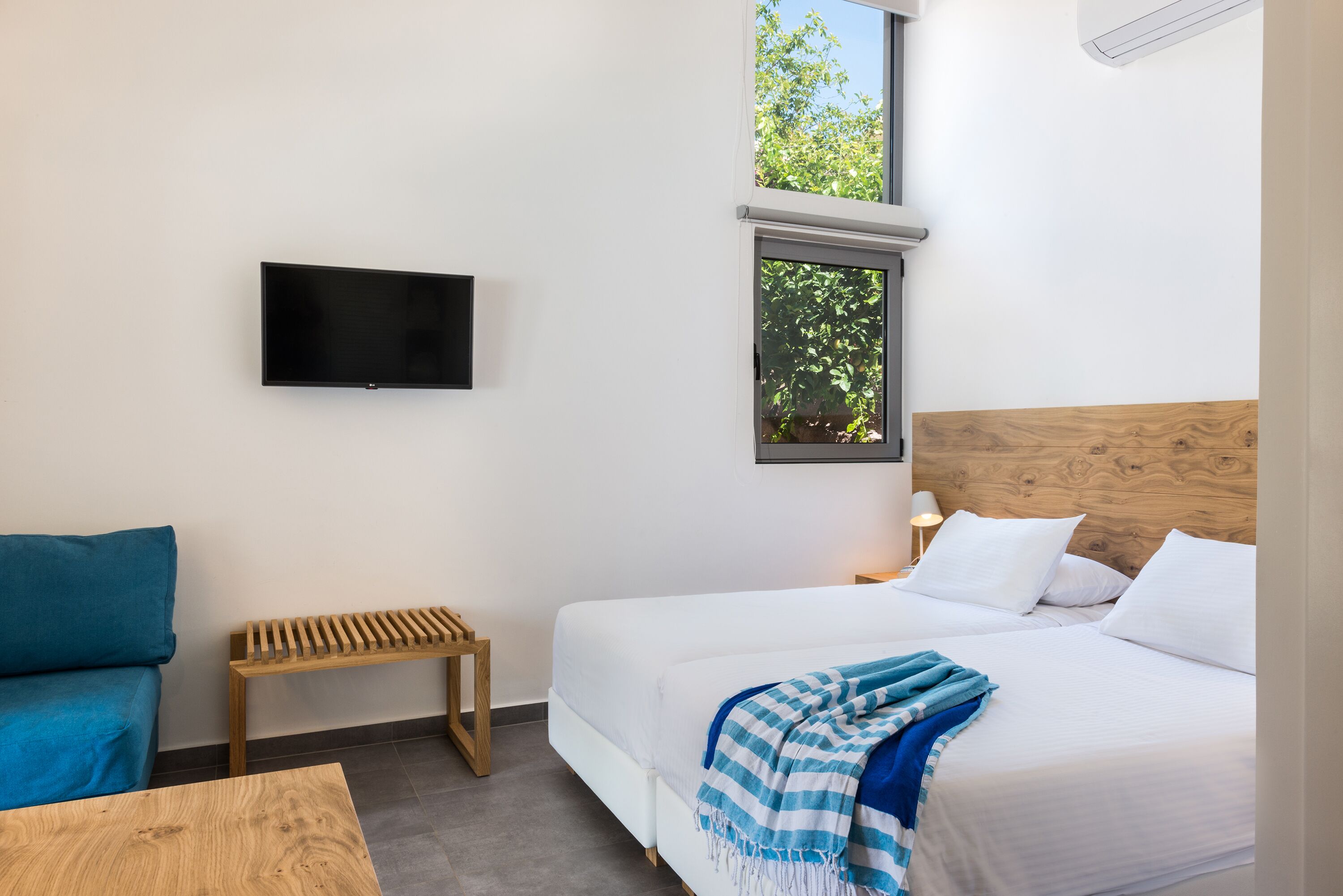A bedroom with a bed, a TV mounted on the wall, a window, and a small table.