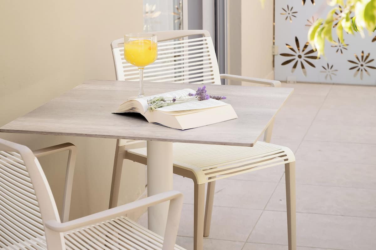 A table with a glass of orange juice, an open book, and a decorative item on a white table.