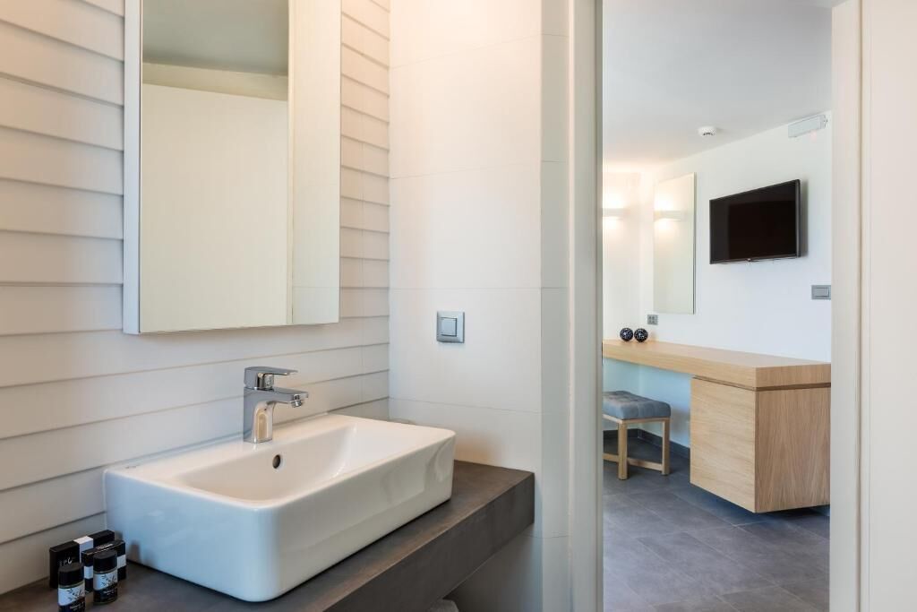 A modern bathroom with a large mirror, a white sink, and a wooden vanity.