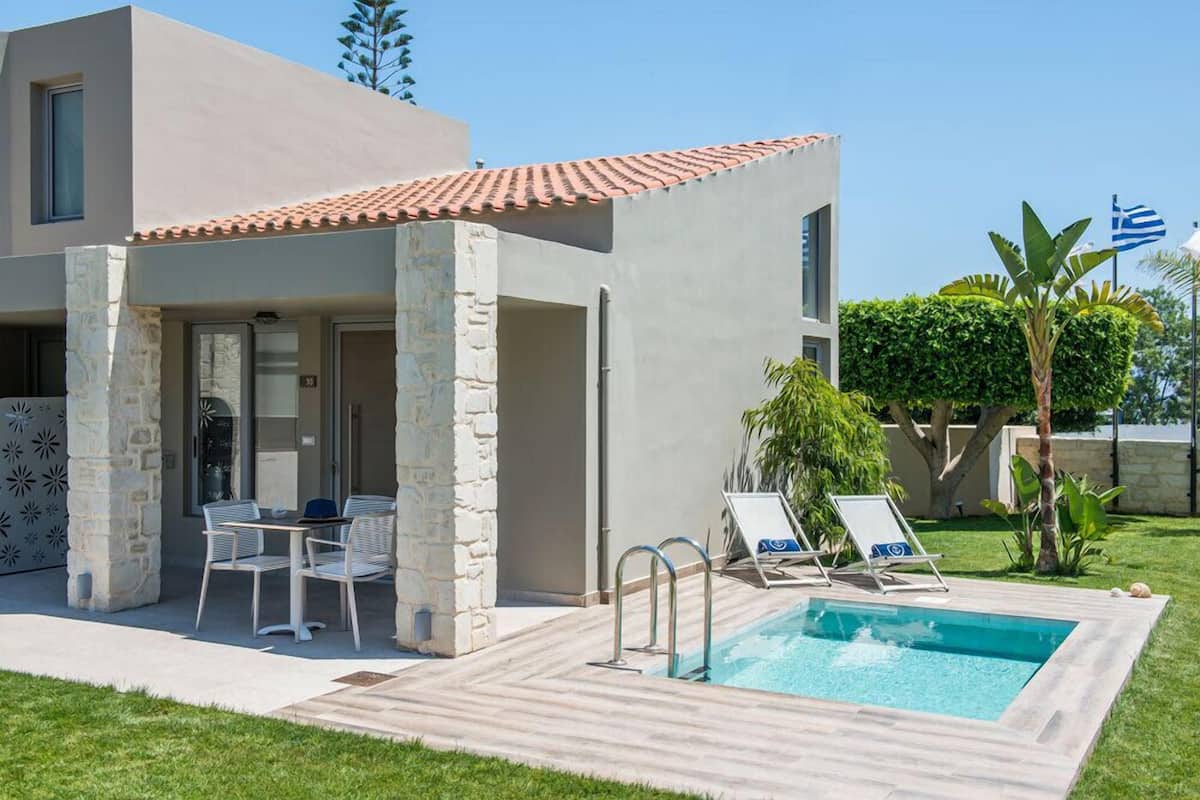 A modern house with a swimming pool, stone pillars, and a patio area with chairs and a table.