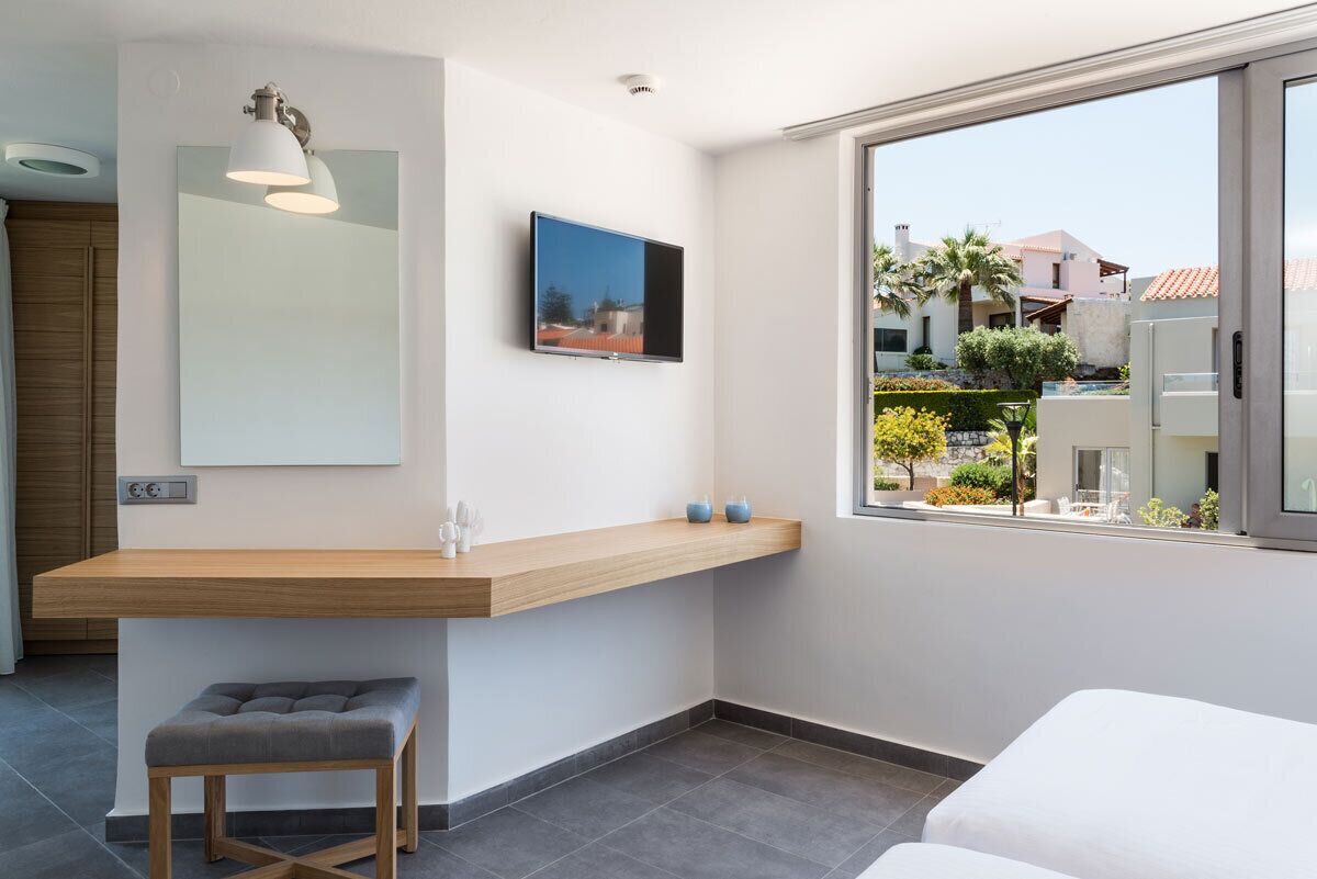 Ein modernes Hotelzimmer mit einem Holztisch, einer grauen gepolsterten Bank, einem großen Spiegel und einem an der Wand montierten Fernseher.