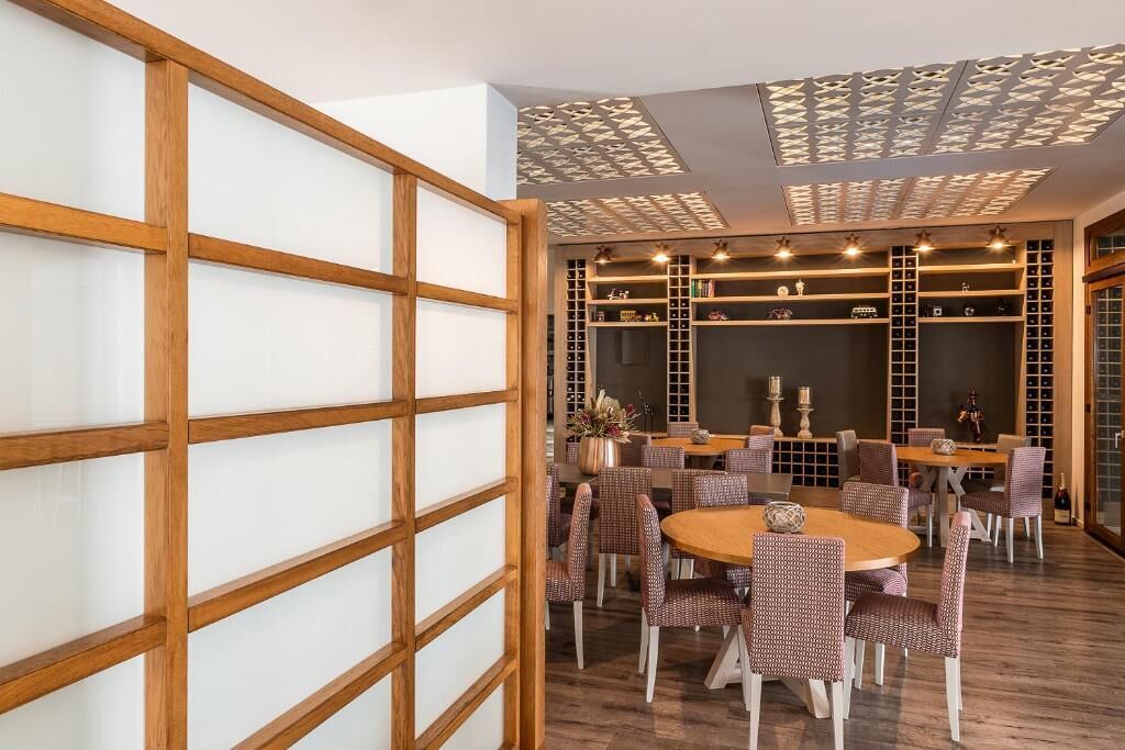 Un coin repas avec une table ronde en bois entourée de chaises à motifs, un plafond décoratif et une bibliothèque contenant divers objets.