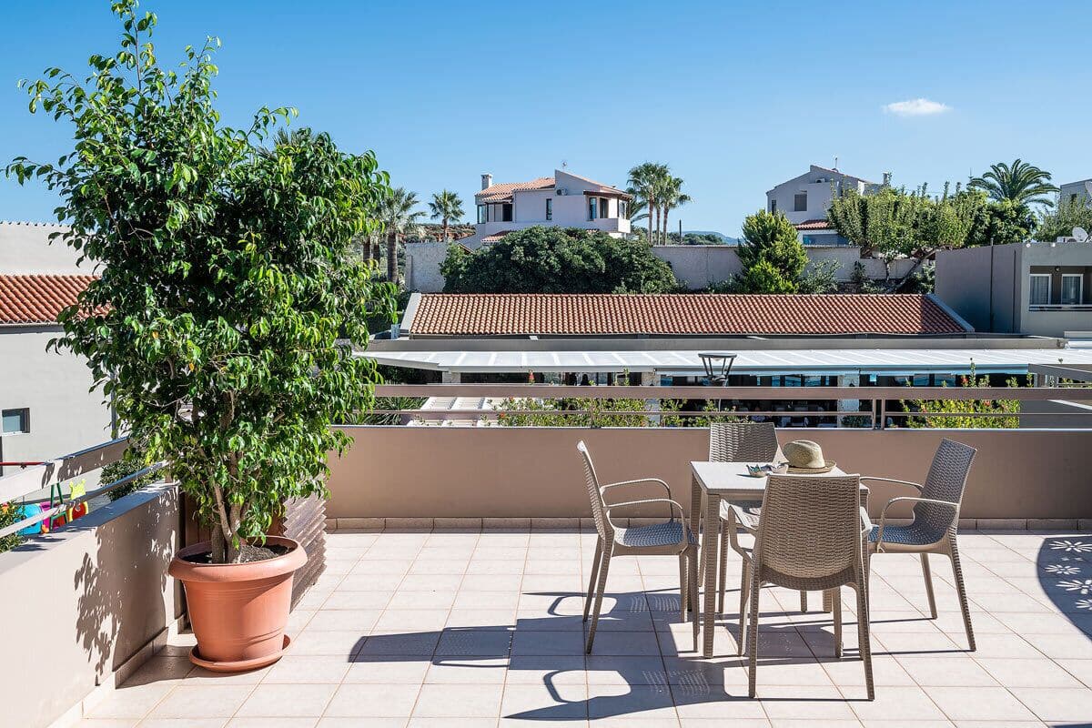 A rooftop terrace with a dining table and chairs, a potted plant, and a view of neighboring buildings.