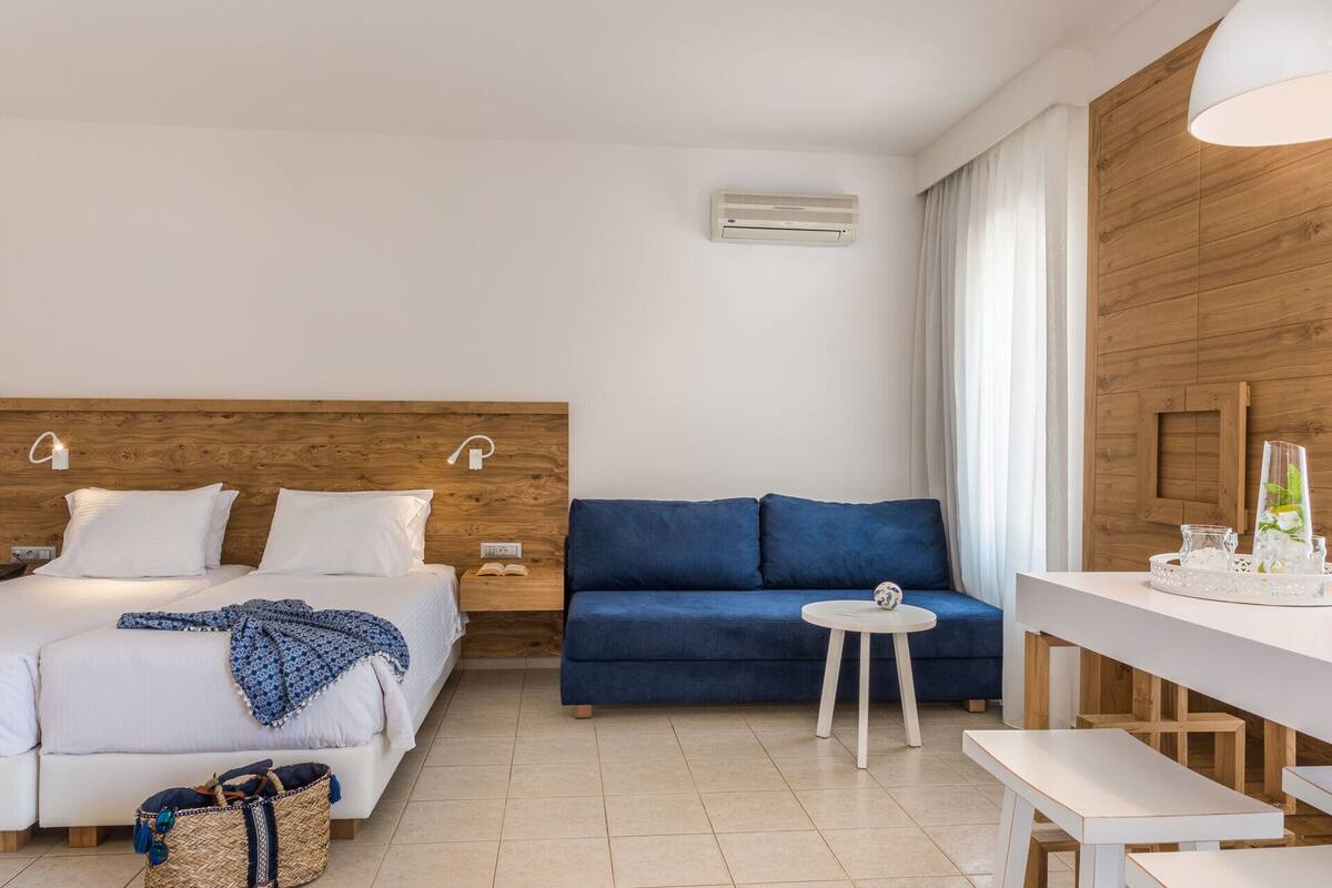 A hotel room with a bed, a blue sofa, a small round table, and a white desk.