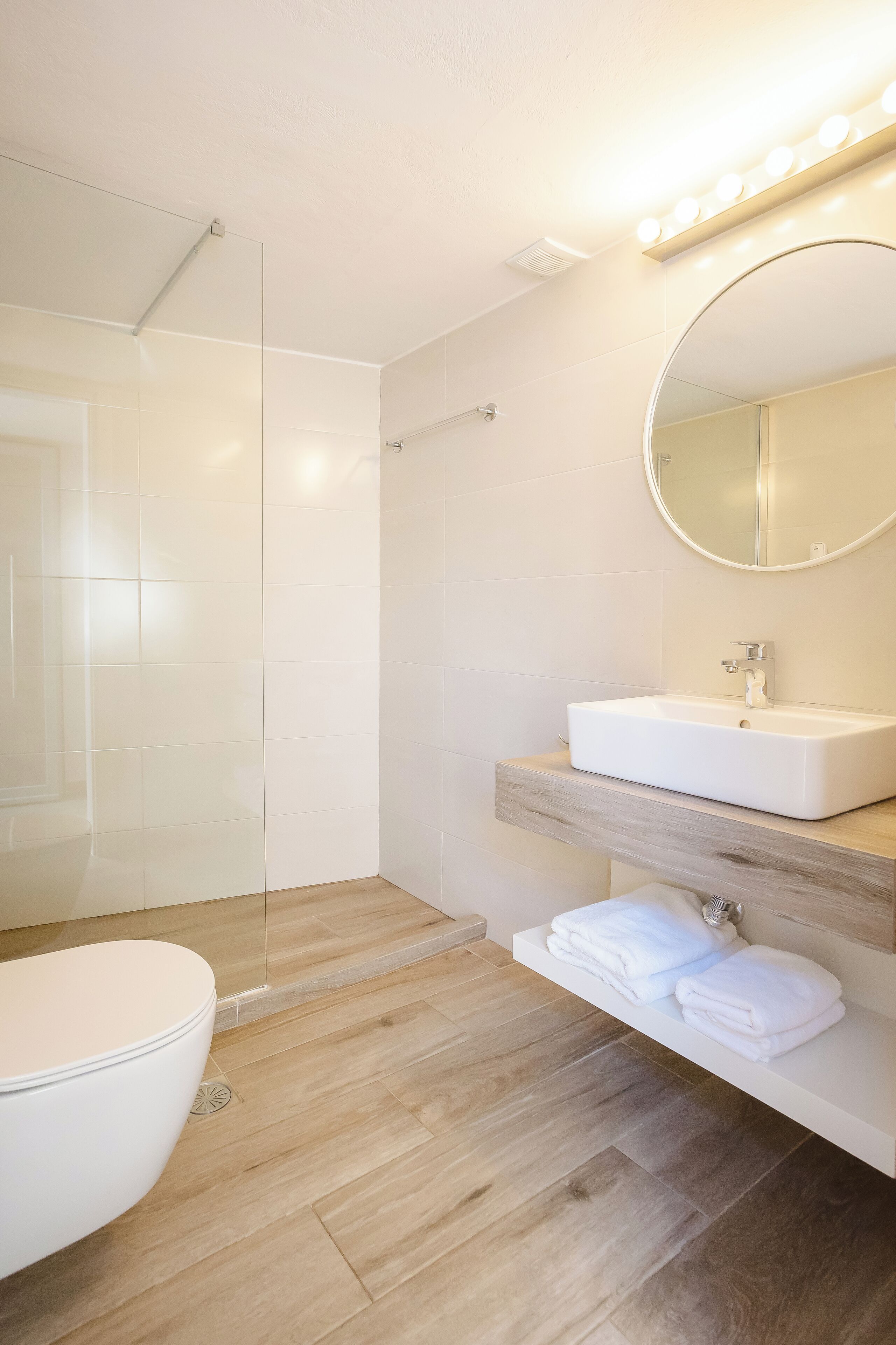A modern bathroom with a glass-enclosed shower, a white sink, and a vanity with towels.