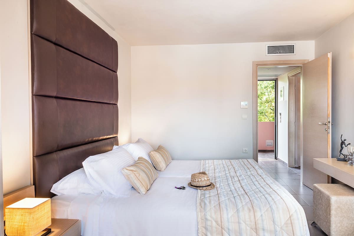 A neatly made bed with a striped bedspread, a bedside lamp, and a hat on the bed.