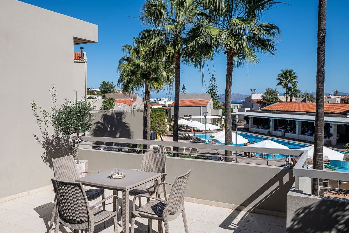 A balcony with wicker furniture, a pool, and palm trees.