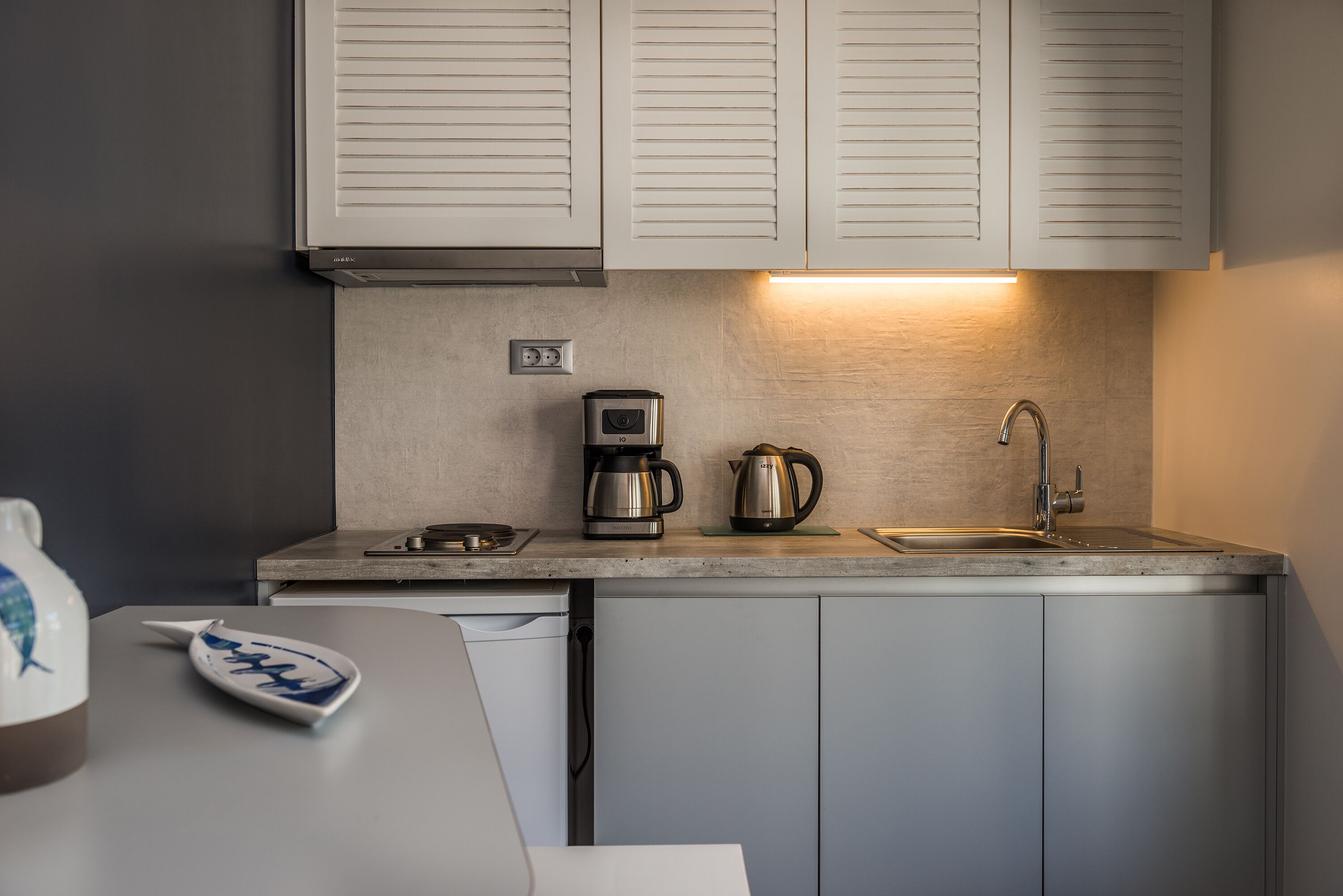 A modern kitchen with a built-in oven, coffee maker, kettle, and sink.