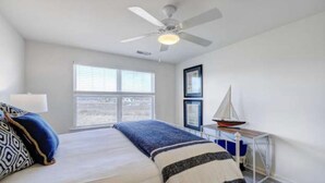 A bedroom with a bed, a ceiling fan, a window with blinds, a sailboat model, and a framed picture on the wall. - Large 4 bedroom penthouse unit 5 miles from Bethany Beach (Ocean View)