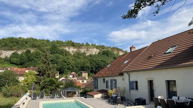 Una piscina con hidromasaje, mobiliario exterior y vistas a una colina con casas.