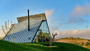 A modern house with a unique geometric roof design, large windows, and a grassy landscape. - 3 Hills Boutique Hotel (Katerini)