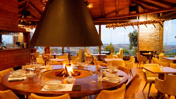 A restaurant with a central fire feature, round tables, and yellow chairs. - 3 Hills Boutique Hotel (Katerini)