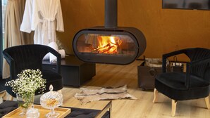 A cozy room with a wood-burning stove, black chairs, a wooden table with a vase of flowers, and a hanging robe. - 3 Hills Boutique Hotel (Katerini)