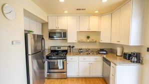 A compact kitchen with white cabinets, stainless steel appliances, and a granite countertop. - Oceanside Beach Rental - Walk to the Boardwalk! (Oceanside)