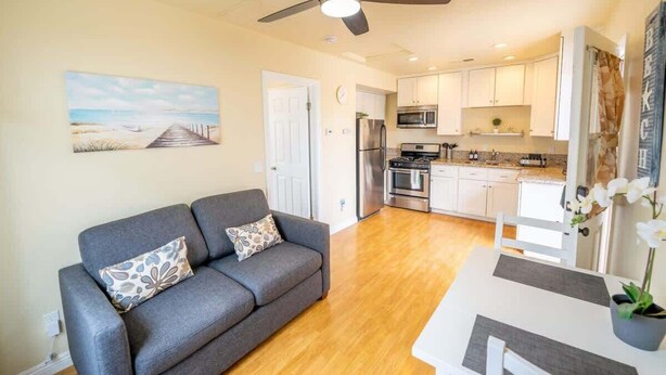 A modern kitchen with white cabinets, stainless steel appliances, and a wooden dining table. - Oceanside Beach Rental - Walk to the Boardwalk! (Oceanside)