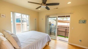 A bedroom with a bed, a ceiling fan, a sliding glass door to a patio, and a small window. - Oceanside Beach Rental - Walk to the Boardwalk! (Oceanside)