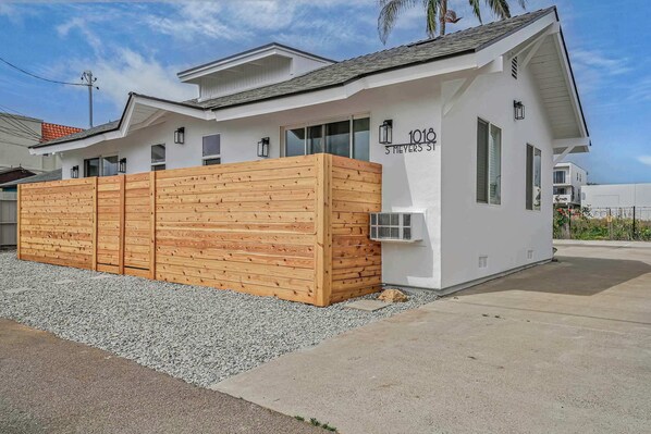 Une maison moderne à deux étages, avec une façade blanche, une clôture en bois et un ciel dégagé.