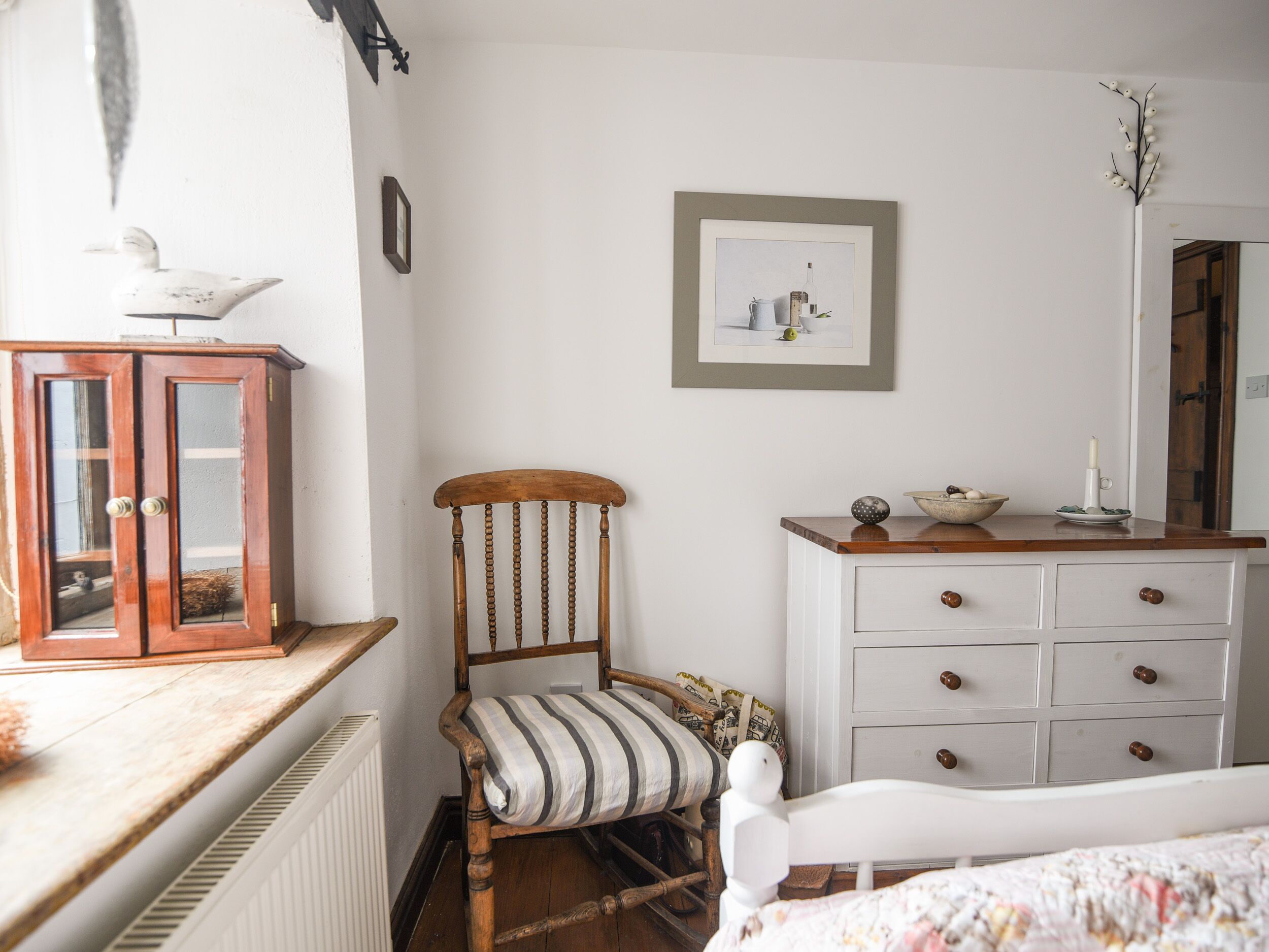 A bedroom with a wooden chair, a white dresser, a framed picture on the wall, and a radiator.