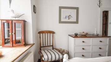 A bedroom with a wooden chair, a white dresser, a framed picture on the wall, and a radiator.