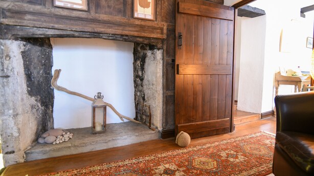 Un interior rústico con una puerta de madera, una chimenea con un farol y una alfombra estampada.