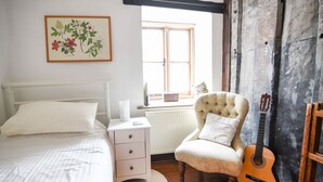 Un dormitorio con una cama, una mesita de noche, una silla y una guitarra.