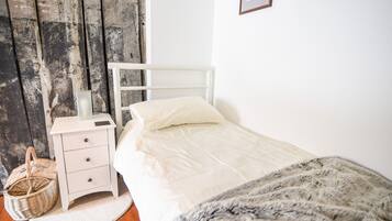 Un dormitorio con una cama blanca, una mesita de noche, una cesta de mimbre y una puerta de madera.