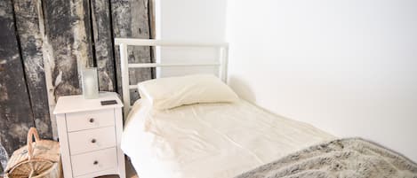 A bedroom with a white bed, a nightstand, a wicker basket, and a wooden door.