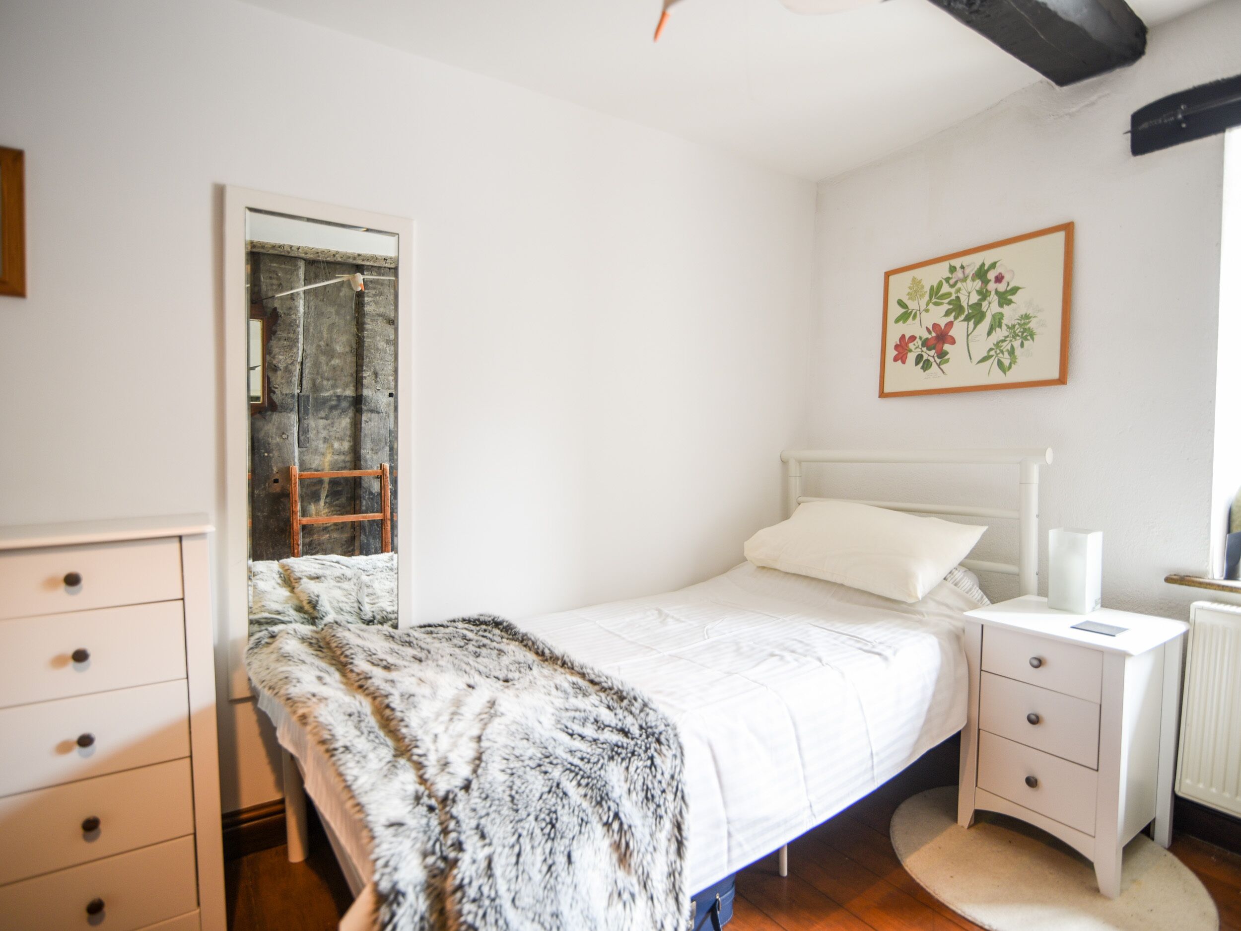 A bedroom with a bed, a bedside table, a nightstand, a dresser, and a mirror.