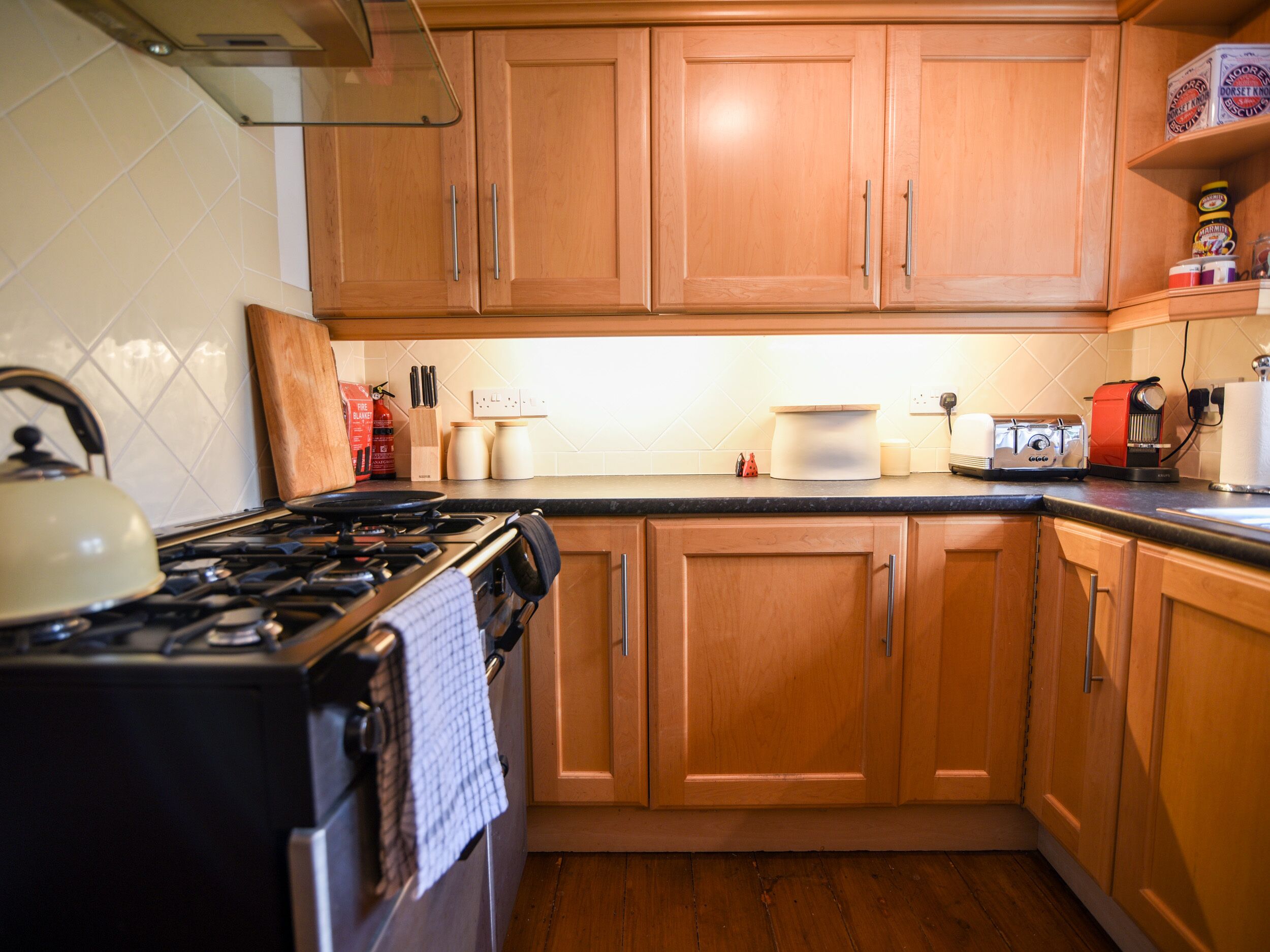 Una cocina con armarios de madera, estufa a gas, tetera y diversos electrodomésticos.
