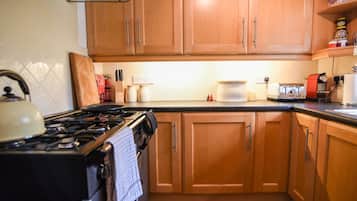 Una cocina con armarios de madera, estufa a gas, tetera y diversos electrodomésticos.