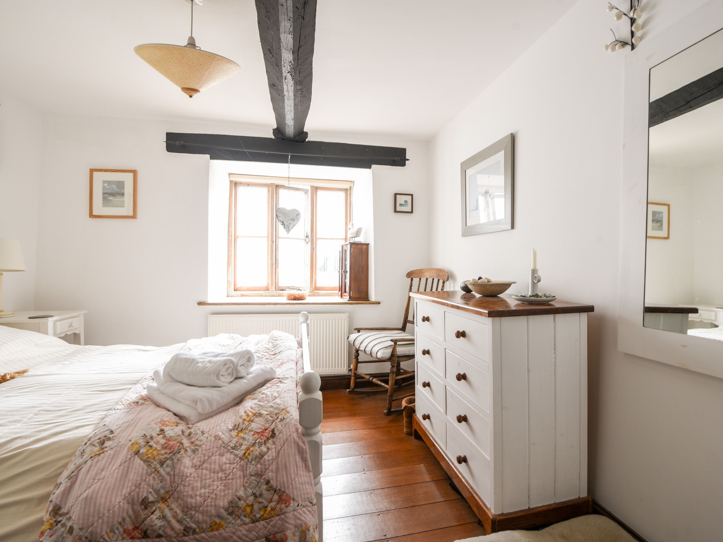 A bedroom with a bed, a dresser, a chair, a window, and a mirror.
