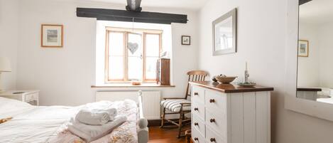 A bedroom with a bed, a dresser, a chair, a window, and a mirror.