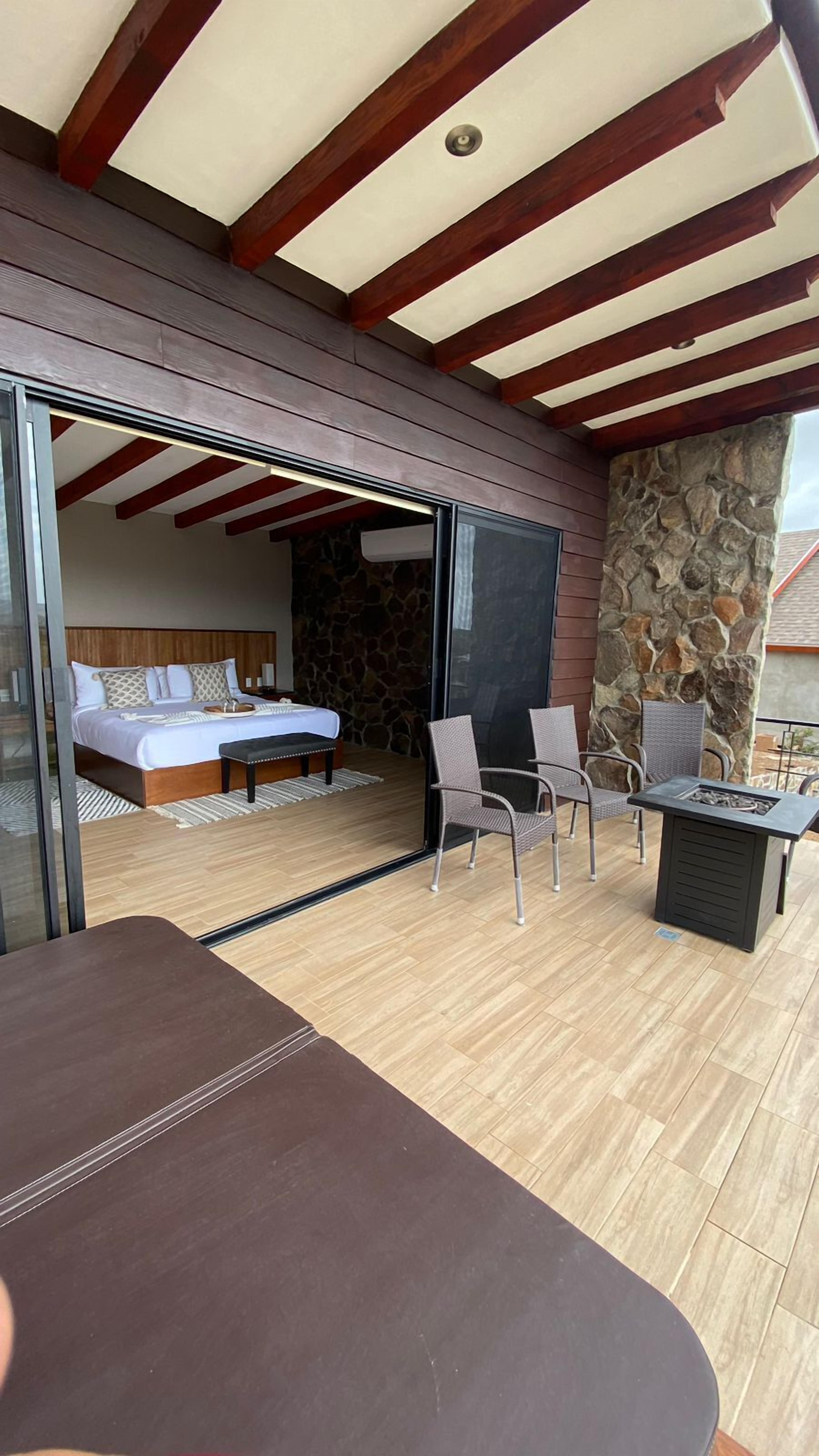 A bedroom with a bed, a nightstand, and a bedside table. There is a stone wall and a wooden ceiling with exposed beams.