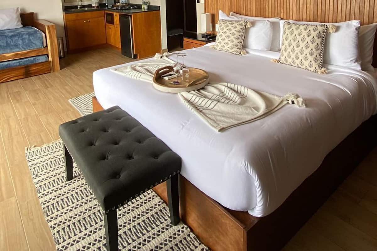 A hotel room with a large bed, a small desk, a chair, and a wooden ceiling.