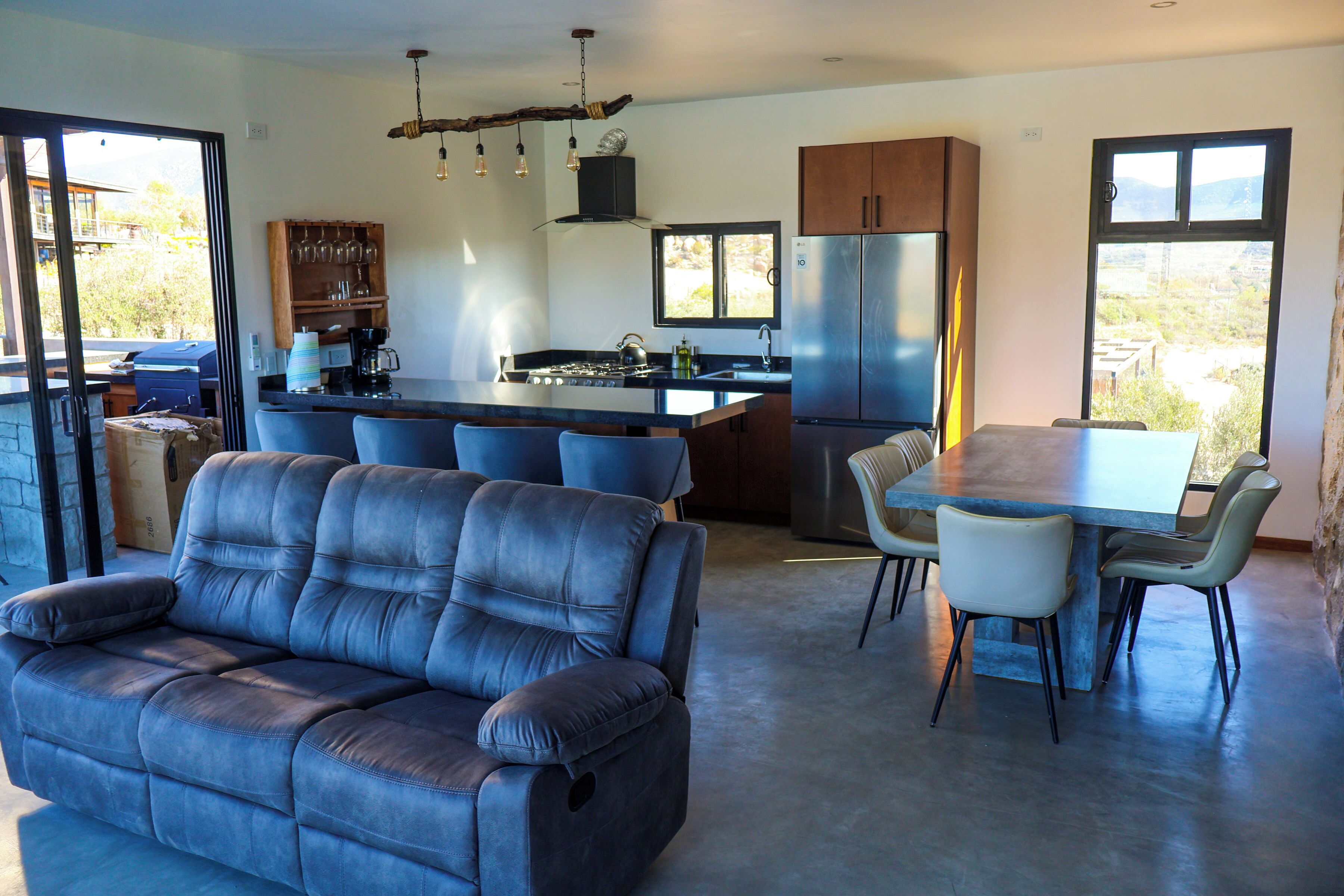 A modern kitchen with a central island, a dining area with a table and chairs, and a seating area with a sofa.