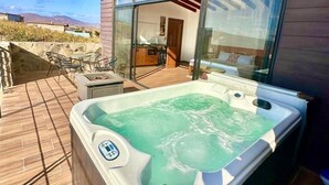 Una bañera de hidromasaje en una terraza de madera con una puerta de vidrio que da a una cocina.