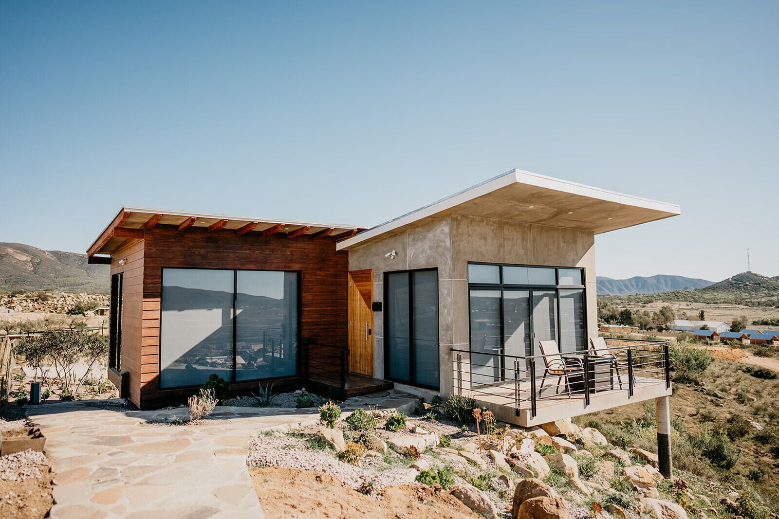 Una casa moderna con un camino de piedra, ventanas grandes y un balcón con sillas.