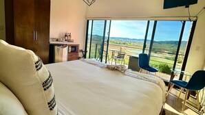 Un dormitorio con una cama grande, televisor montado en la pared y balcón con vistas al campo.