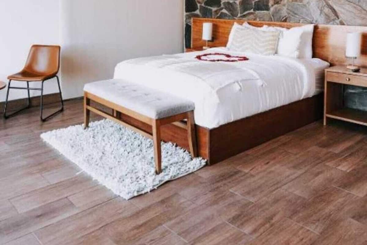 A bedroom with a stone wall, wooden beams, a bed with white bedding, a bench, and a chair.