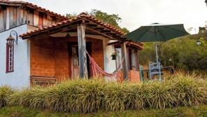 A rustic house with a tiled roof, a hammock, and a large umbrella. - Serra a vista chalés (Prados)